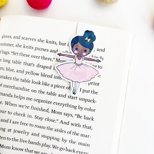 May include: A pink ballerina bookmark with a black girl wearing a pink tutu and a white bow in her hair. The bookmark is holding a pink and white balloon. The text "I put the print" is visible on the bookmark.