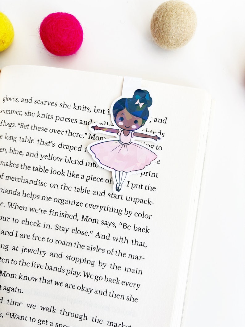 May include: A pink ballerina bookmark with a black girl wearing a pink tutu and a white bow in her hair. The bookmark is holding a pink and white balloon. The text "I put the print" is visible on the bookmark.