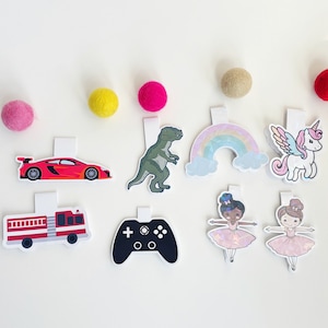 May include: A set of ten colorful bookmarks featuring various designs, including a red race car, a green dinosaur, a rainbow, a unicorn, a fire truck, a video game controller, and two ballerinas.