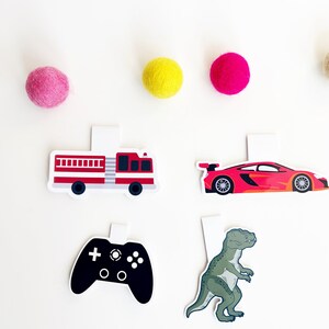 May include: Four colorful paper bookmarks with different designs: a red fire truck, a red sports car, a black video game controller, and a green dinosaur.