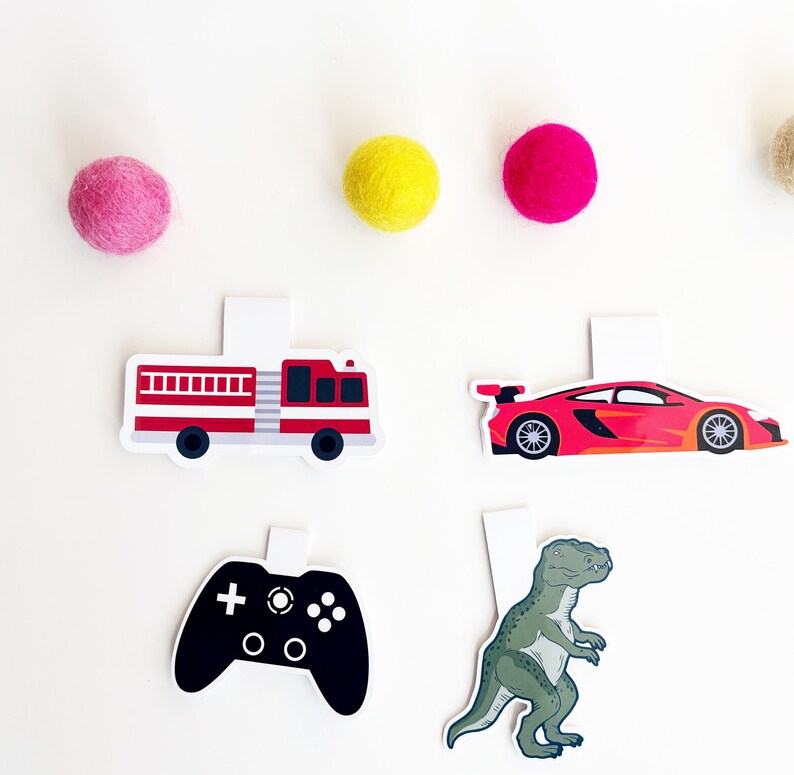May include: Four colorful paper bookmarks with different designs: a red fire truck, a red sports car, a black video game controller, and a green dinosaur.