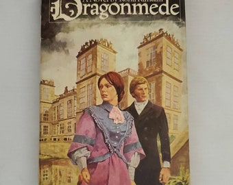 May include: A book cover with a vintage illustration of a couple standing in front of a large, stone building. The book title is "Dragonmede" and the author is "Rona Randall".