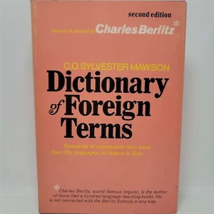 May include: A pink book cover with the title "Dictionary of Foreign Terms" in black text. The book is a second edition and was revised and updated by Charles Berlitz. The book contains thousands of expressions from more than fifty languages, from Afrikaans to Zulu.