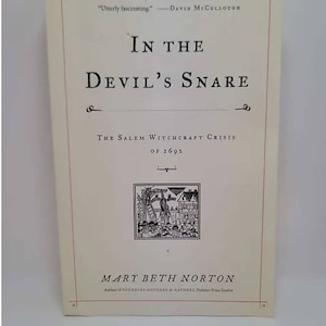 May include: Book cover with the title "In the Devil's Snare: The Salem Witchcraft Crisis of 1692" by Mary Beth Norton. The cover is white with black text and a black and white illustration of a scene from the Salem Witch Trials.
