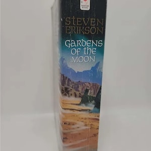 K&ouml;nnte beinhalten: Ein Taschenbuch mit dem Titel "G&auml;rten des Mondes" von Steven Erikson. Der Buchumschlag zeigt eine Landschaft mit einer W&uuml;stenlandschaft und einer gro&szlig;en Felsformation.