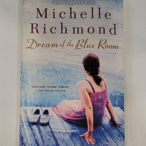 May include: Book cover for "Dream of the Blue Room" by Michelle Richmond, a novel. The cover features a woman in a pink dress sitting on a wooden dock. The text "INTELLIGENT, ORIGINAL, COMPLEX." is printed on the cover.
