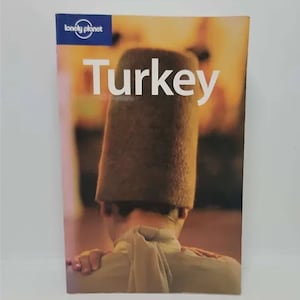 May include: A Lonely Planet guidebook for Turkey with a photo of a person wearing a traditional Turkish hat.