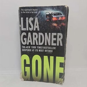 May include: A paperback book cover with a black background and a green title that reads "GONE". The author's name, "LISA GARDNER", is printed in white above the title. The book cover features a car driving on a rainy road at night.