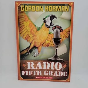 May include: A book cover with an orange background and a yellow and green parrot with a microphone. The title is "Radio Fifth Grade" by Gordon Korman. The book is published by Scholastic.