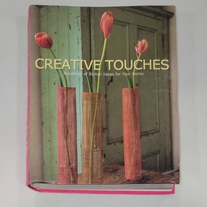 May include: A book titled "Creative Touches: Hundreds of Stylish Ideas for Your Home" with a photo of three vases with pink flowers on the cover.