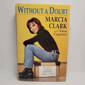 May include: A book titled "Without a Doubt" by Marcia Clark with Teresa Carpenter. The cover features a photo of Marcia Clark sitting on a box labeled "People v. Simpson BA097211 Box __ of __".