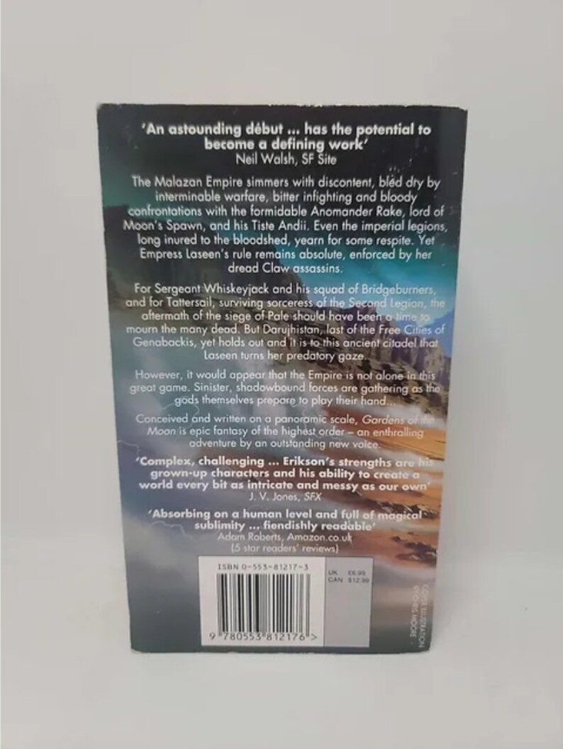 K&ouml;nnte beinhalten: Ein Buchcover mit dunkelblauem Hintergrund und einem wei&szlig;en und goldenen Design. Der Titel des Buches lautet "Gardens of the Moon" und der Autor ist Steven Erikson. Das Buch wird als "epische Fantasy vom h&ouml;chsten Niveau" und "ein fesselndes Abenteuer von einer herausragenden neuen Stimme" beschrieben.