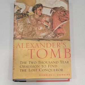 May include: A book cover with a painting of a man on a horse. The title of the book is "Alexander's Tomb: The Two Thousand Year Obsession to Find the Lost Conqueror" by Nicholas J. Saunders.
