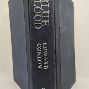 May include: A hardcover book titled "BLUE BLOOD" by Edward Conlon. The book has a dark blue cover with the title and author's name in silver lettering. The Riverhead Books logo is visible.