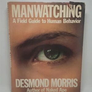 May include: A book cover with the title "Manwatching: A Field Guide to Human Behavior" by Desmond Morris, author of "Naked Ape". The cover features a close-up of a person's eye.