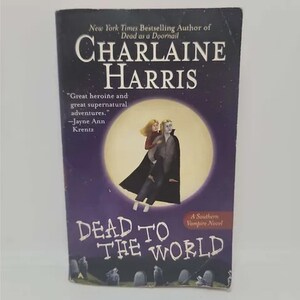 May include: A paperback book titled "Dead to the World" by Charlaine Harris. The cover features a purple background with a full moon and an illustration of two figures. The book is a Southern Vampire Novel.