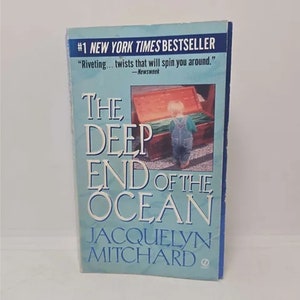 May include: A book cover with a blue background and the title "The Deep End of the Ocean" by Jacquelyn Mitchard. The cover features a young child standing in front of a wooden chest.