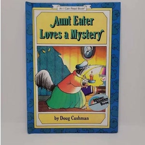 May include: A blue book cover with a cartoon illustration of an anteater holding a candle. The title of the book is "Aunt Eater Loves a Mystery" and the author is Doug Cushman. The book is part of the Reading Rainbow Book series.