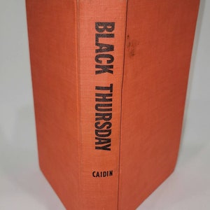 May include: A hardcover book titled "BLACK THURSDAY" by Caidin, published by Dutton. The book has a bright orange cover and spine, with the title and author's name printed in black. The book is standing upright.
