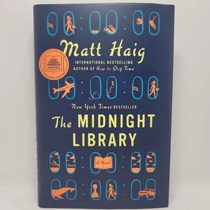May include: A blue book cover with the title "The Midnight Library" by Matt Haig, an international bestselling author. The cover features a clock face with various symbols and the GoodReads logo.