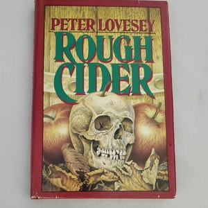 May include: A red hardcover book with the title "Rough Cider" by Peter Lovesey. The cover features a skull with apples and leaves.