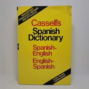May include: A yellow hardcover book titled "Cassell's Spanish Dictionary" with the words "Spanish-English" and "English-Spanish" printed in black. The book has a black sticker on the bottom right corner that says "Over 750,000 Copies Sold".