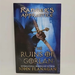 May include: A book cover with a blue background featuring a hand holding a bow and arrow. The title is "Ranger's Apprentice: The Ruins of Gorlan" by John Flanagan.