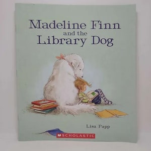 May include: A book cover with a light green background featuring a white dog and a girl reading a book. The title is "Madeline Finn and the Library Dog" by Lisa Papp. The Scholastic logo is at the bottom of the cover.