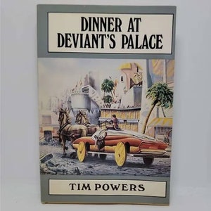May include: A book cover with a gray background and the title "Dinner at Deviant's Palace" in black text. The cover features a colorful illustration of a futuristic vehicle with horses pulling a carriage in a city setting. The author's name, "Tim Powers", is printed in white text on a gray background at the bottom of the cover.
