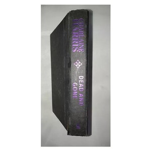 May include: A black hardcover book with the title "Dead and Gone" by Charlaine Harris on the spine.