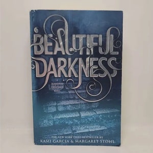 May include: A blue paperback book with the title "Beautiful Darkness" in silver lettering. It is a "Beautiful Creatures" novel and a New York Times bestseller by Kami Garcia & Margaret Stohl.