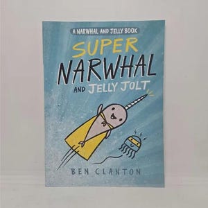 May include: A blue book cover with the title "Super Narwhal and Jelly Jolt" in yellow and black text. The cover features a cartoon narwhal wearing a yellow cape and a cartoon jellyfish.