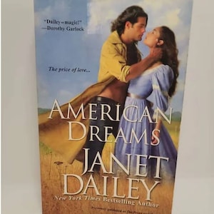 May include: Book cover featuring a couple embracing in a field. The title is "American Dreams" by Janet Dailey, a New York Times bestselling author. The quote "Dailey - magic!" by Dorothy Garlock is featured on the cover.