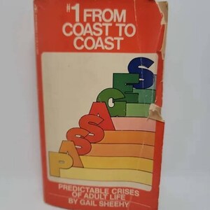 May include: A red paperback book with the title "#1 From Coast to Coast Passages Predictable Crises of Adult Life by Gail Sheehy". The cover features a colorful graphic of the word "Passages" in a rainbow color scheme.