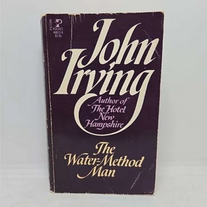 May include: A purple paperback book with the title "The Water-Method Man" by John Irving. The book cover features the author's name in large, stylized font and includes the text "Author of The Hotel New Hampshire".