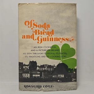 May include: A vintage book cover with the title "Of Soda Bread and Guinness" in orange text. The subtitle is "An Irish Cookbook, and a Picture of Ireland as seen through its people, its places, its traditions and its cooking lore". The cover features a black and white photo of a cityscape with a green shamrock in the corner.