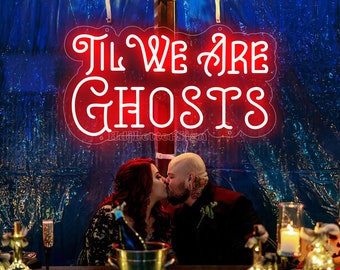May include: A red neon sign with the text "Til We Are Ghosts" hanging on a blue wall. A couple is kissing in front of the sign.