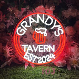 May include: A white neon sign with a red outline in the shape of a circle. The sign says "Grandy's Tavern Est 2024" and features a beer mug with foam on top.