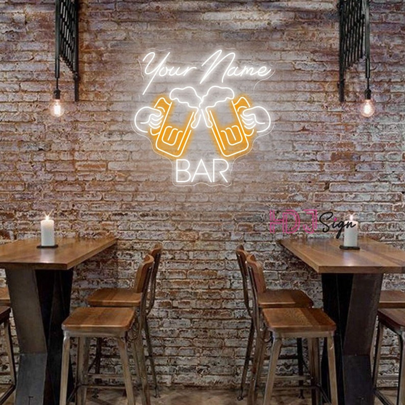 Op de afbeelding: Neon-bord met twee bierglazen die klinken, met de tekst "Your Name BAR" in wit. Het bord is gemonteerd op een bakstenen muur in een bar-omgeving.