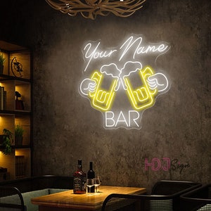Op de afbeelding: Neon-bord met de tekst "Your Name Bar" in wit met twee gele bierglazen die klinken.
