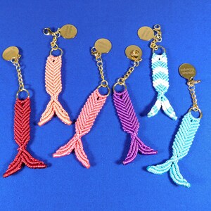 May include: Seven colorful fishtail keychains with gold chains and round metal tags. The keychains are made of braided string in shades of pink, red, purple, blue, and white.