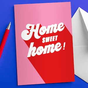 Tarjeta de felicitación de inauguración de la casa con tipografía moderna, letras rosas y rojas, tamaño A6