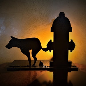 May include: A black silhouette of a dog peeing on a fire hydrant. The dog is facing left and the hydrant is facing right. The dog is on a black base and the hydrant is on a black base. The dog is in the foreground and the hydrant is in the background. The dog is in the shape of a silhouette and the hydrant is in the shape of a silhouette.