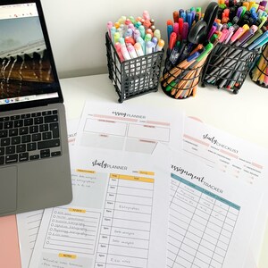 以下が含まれることがあります： 黄色と白のグリッド、やることリスト、メモ欄のある学習プランナー。プランナーはピンクの表面に置かれ、ラップトップとカラフルなペンとマーカーの入った3つの容器がある。