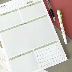 May include: A white planner with a green header that says "Planner". The planner is divided into sections for facts and ideas, introduction, main body, conclusion, and to do. There is a black pen and a green highlighter on top of the planner.