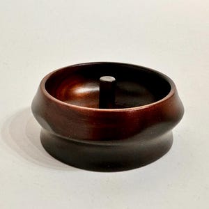 May include: A dark brown wooden bowl with a small knob in the center. The bowl has a rounded shape and a smooth finish.