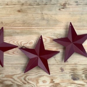 May include: Three burgundy metal star-shaped ornaments on a wooden surface.