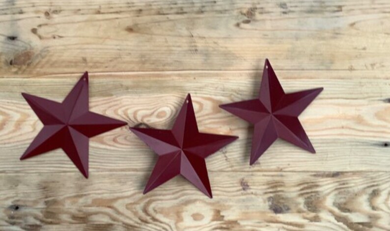 May include: Three burgundy metal star-shaped ornaments on a wooden surface.