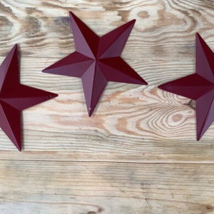 May include: Three red metal star shapes on a light brown wooden background.
