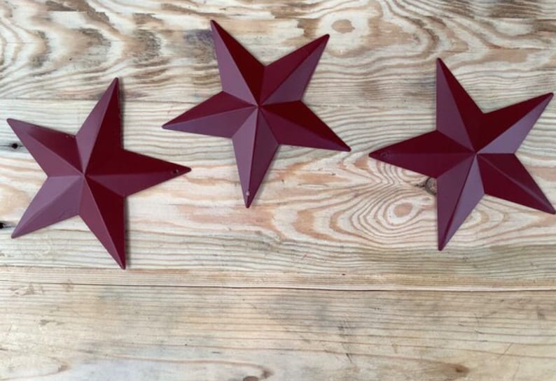 May include: Three red metal star shapes on a light brown wooden background.
